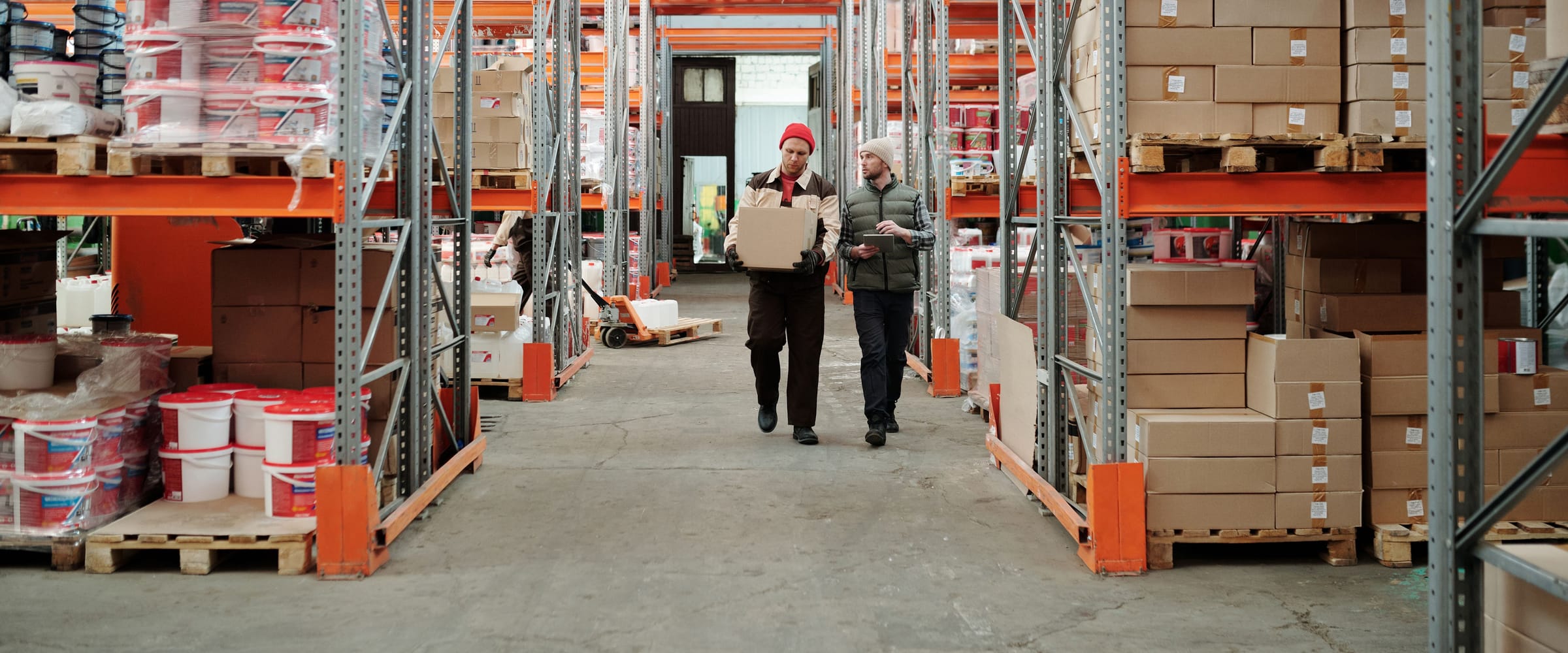 Warehouse staff carrying stock and checking records between the racks